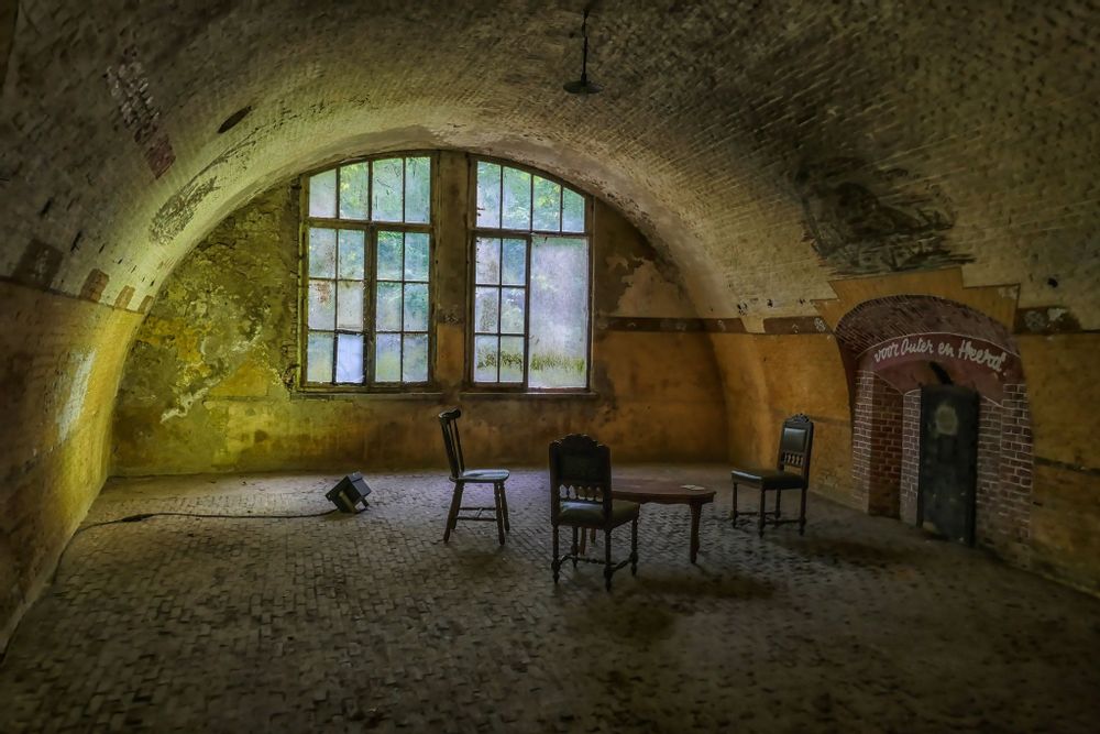 Inside Fort 5 bunker, Antwerpen. There are 3 green chairs. Above a small door, it reads “Voor Outer en Heerd”
