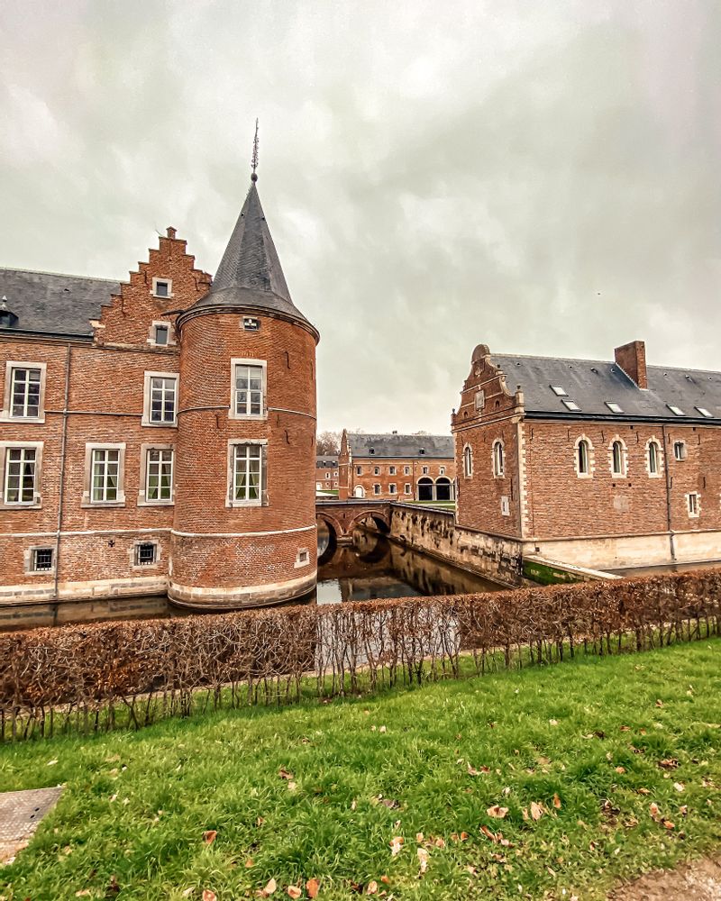 The red brick buildings of the Alden Biesen castle complex sit next to each other separated by a moat in Bilzen, Belgium.