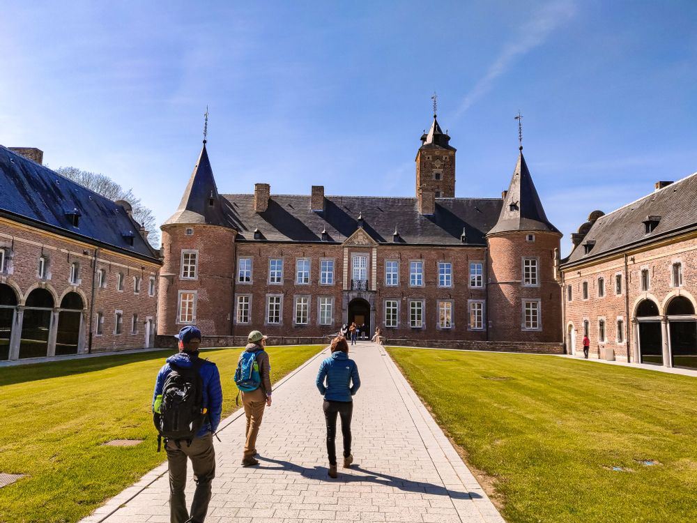 Three travellers wearing backpacks walking towards castle Alden Bisen, Belgium