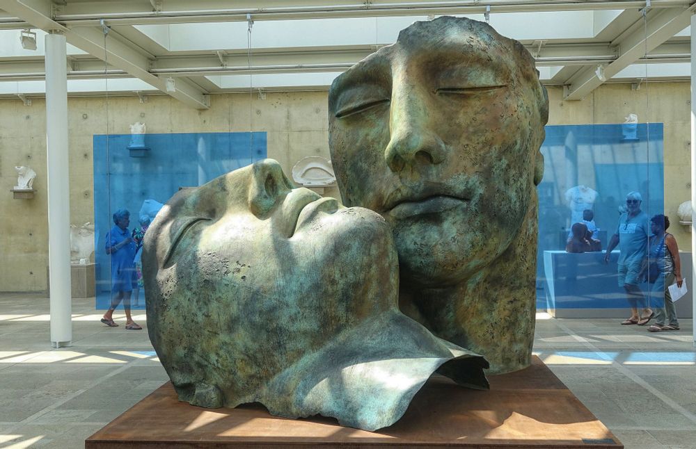 Museum visitors walk behind a green set of statue heads in Beelden aan Zee. 