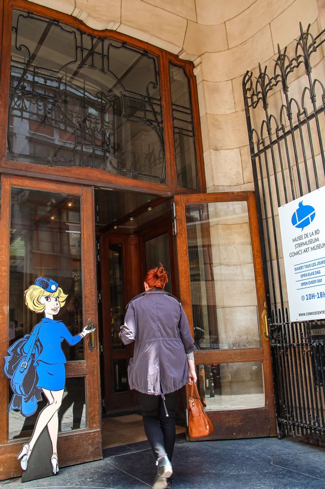 A visitor walks into the open door at the entrance of the Comics Art Museum in Brussels, an image of a lifesize comic character walking in is on the closed door to the left