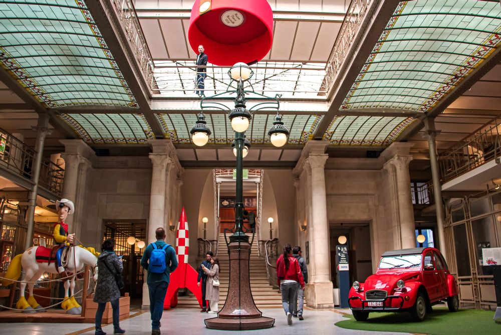 The entrace hall of the Comics Art Museum in Brussels with lifesize models of comic characters, a rocket and a car, along with guests walking through the hall