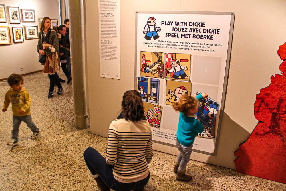 A woman sitting on the floor as her child plays with a game on the wall of the Comics Art Museum, Brussels
