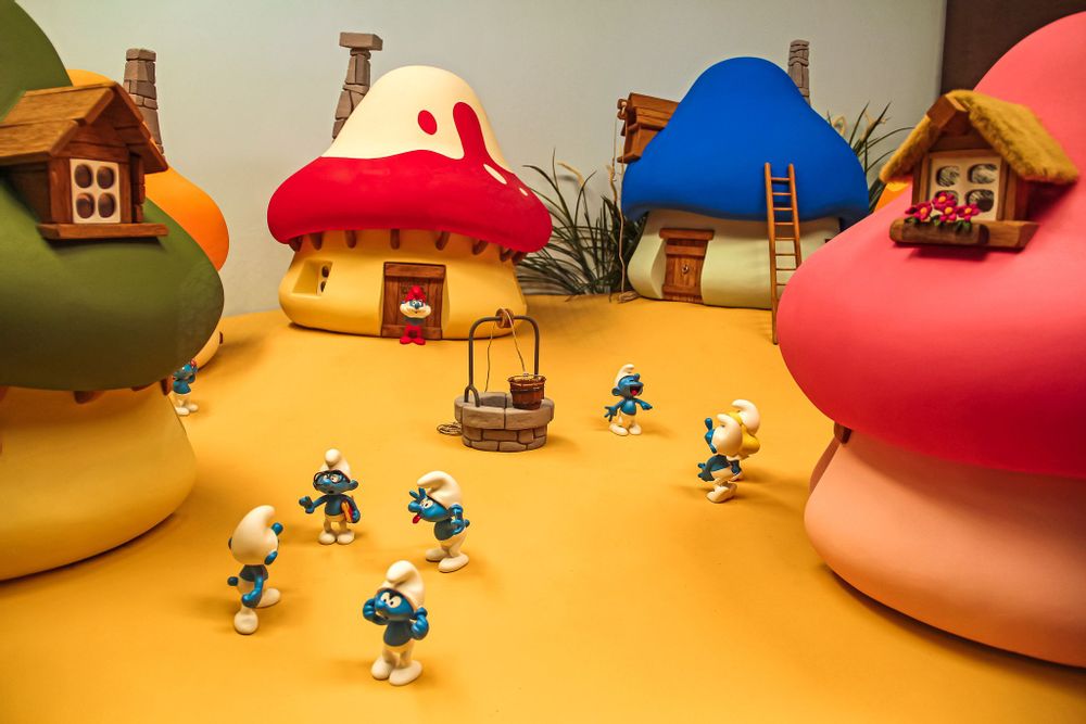 A miniature toy smurf village with four mushroom houses and a group of smurfs in the centre
