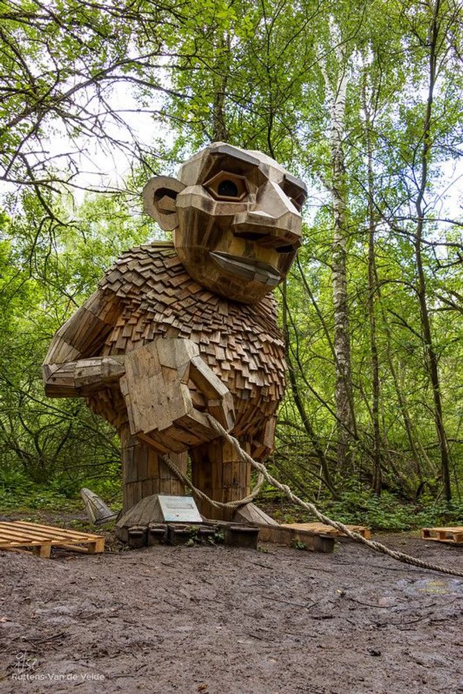 Wooden troll sculpture holding a rope on a muddy walking trail in De Schorre, Antwerp