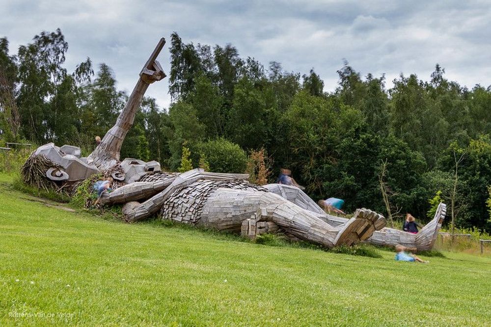 Two wooden troll sculptures lying down on the grass in De Schorre park, Antwerp