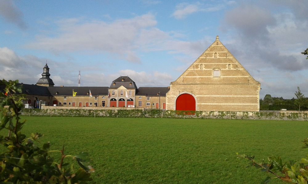 The brick buildings and red doors of Herkenrode Abbey in Hasselt, Belgium, sits at the end of a green field.