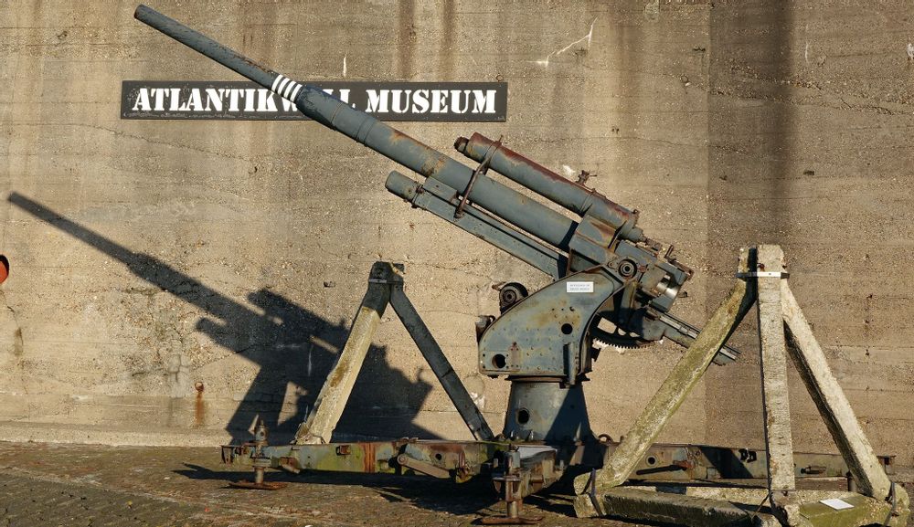 A rusted gun from WW2 rests before the sign for the Atlantic Wall Museum 