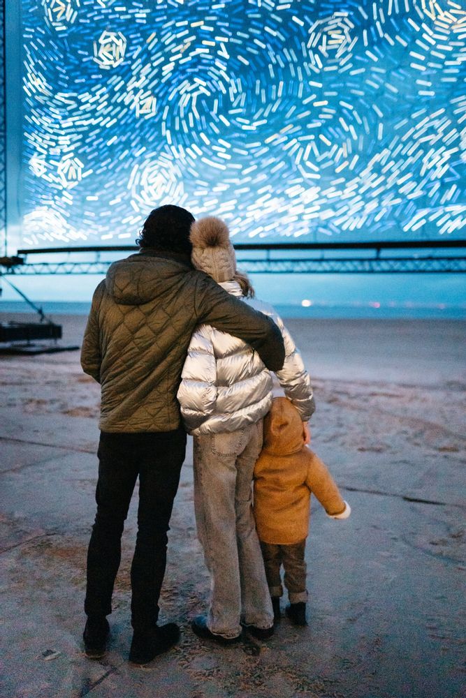 Family of three, couple and child, on the harbour. Starry Night light display at the Light ART festival, Knokke-Heist