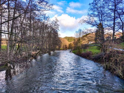 Wide, choppy river lined by trees in winter along the Ourtal Route, Belgium