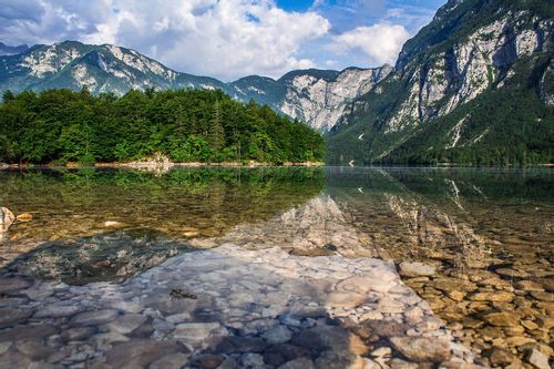 Lake Bohinj and its clear waters with pebbles and rocks amongst the mountains.
