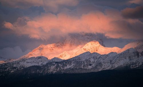 The top of Mount Triglav lit up by the setting sunlight between the clouds.