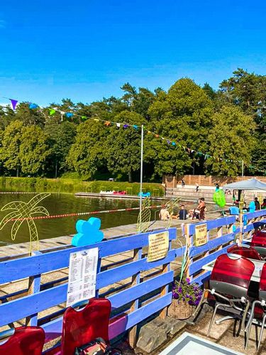 A view of Lake Conchibois from the café, with a blue fence in the foreground and people sitting beside the lake in the background.