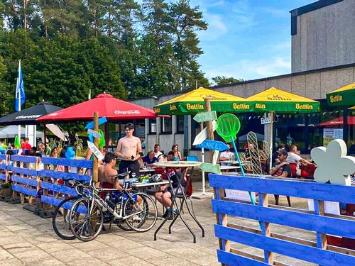 The café at Lake Conchibois with branded umbrellas and people sitting at tables behind a blue fence.