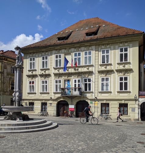 A historical building on Stari Trg with a cyclist biking through the street.